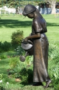 Larger than life-size sculpture of a girl watering flowers.
